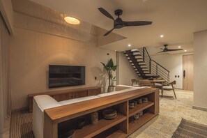 Un salon moderne doté d’un téléviseur à écran plat, d’un meuble de rangement en bois et d’un escalier menant à un niveau supérieur.