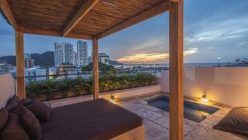 Ein Balkon mit einer Holz-Pergola, einem kleinen Pool und einer Sitzecke mit Kissen.