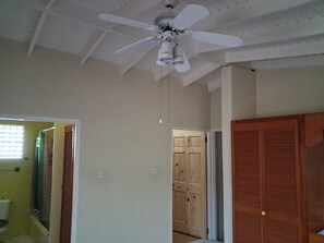 Ein Zimmer mit Deckenventilator, Holztüren und einem Fenster mit Jalousien.