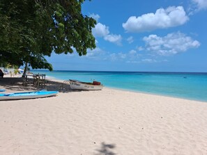 Una playa con cielo despejado, mar tranquilo y un bote llamado 'D. WAVEY' en la arena.