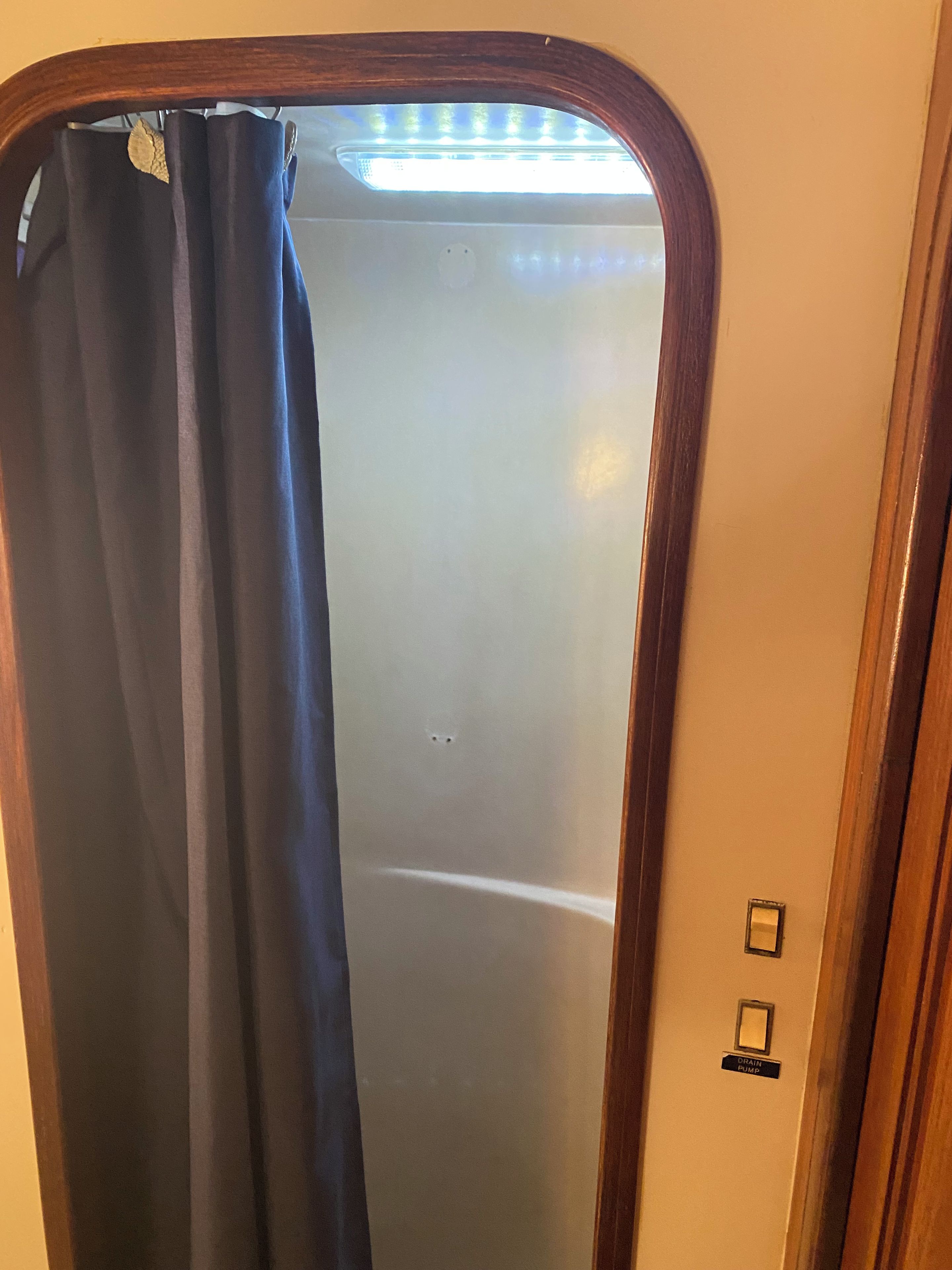 Ein Badezimmer mit Duschvorhang, einer Deckenleuchte und einem an der Wand montierten Lichtschalter.
