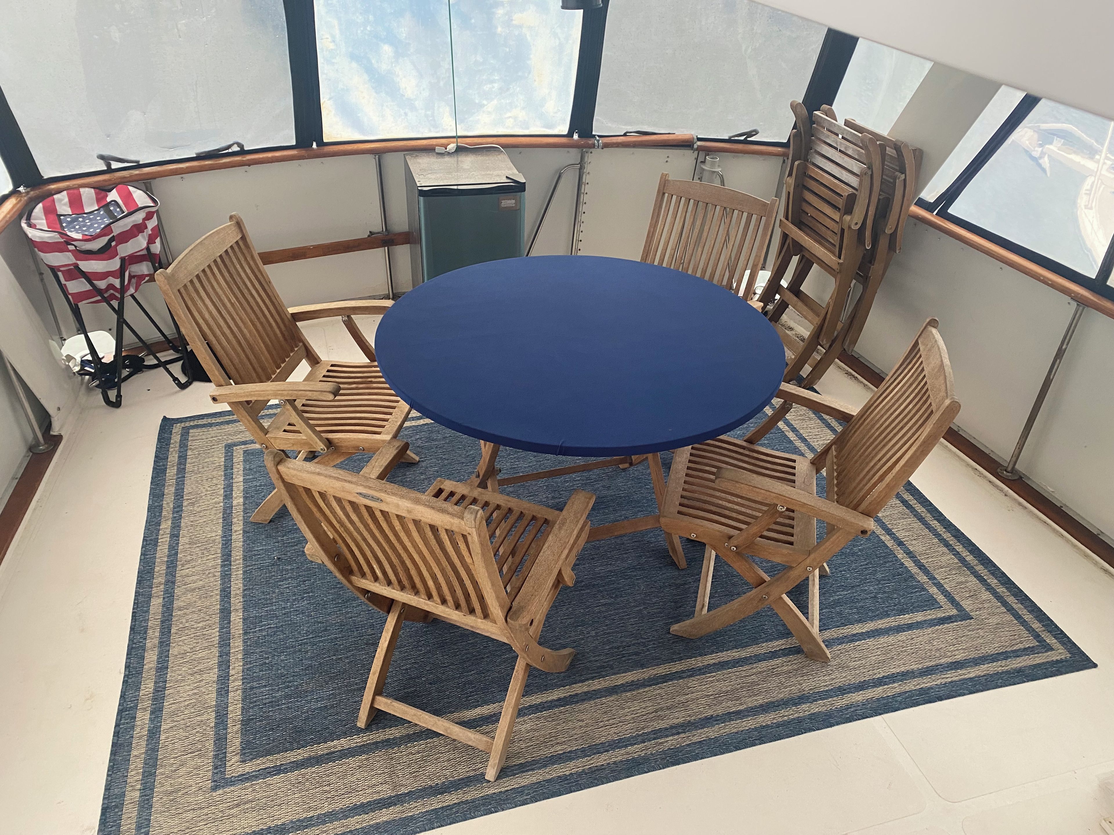 A round table with six wooden chairs, a blue rug, and a window with a view of the sky.