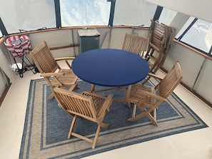 A round table with six wooden chairs, a blue rug, and a window with a view of the sky.