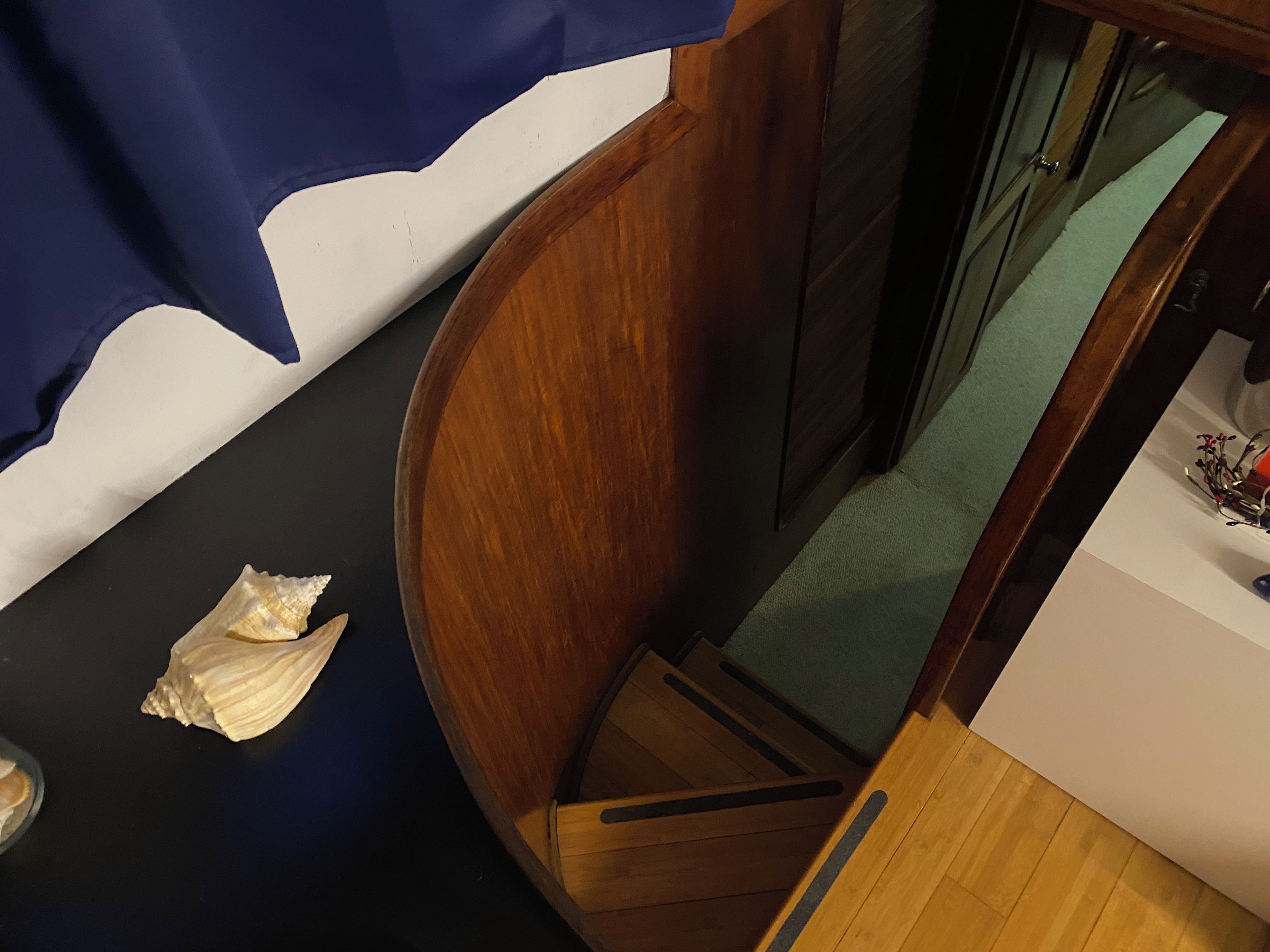 Una escalera de madera con una cortina azul, una pared blanca y un pequeño objeto blanco en el suelo.