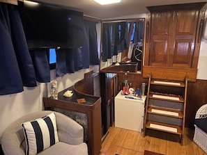 A compact living space with a television, a small refrigerator, a wooden cabinet, and a cushioned chair.