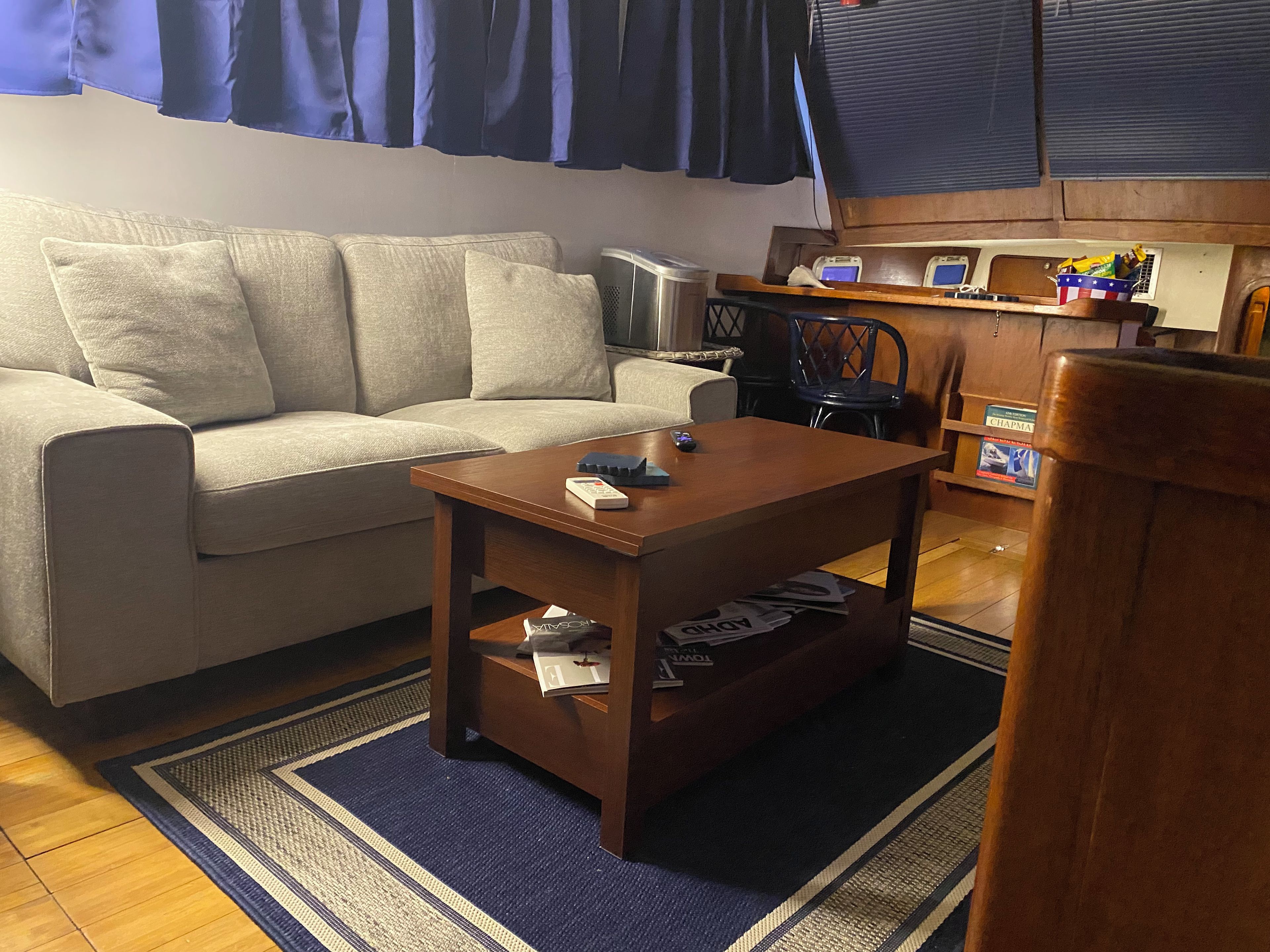 Una sala de estar con sofá, una mesa de centro, televisor y una zona de cocina con microondas y un libro.