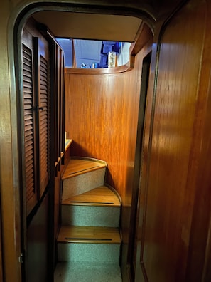 A narrow wooden staircase with a carpeted landing, leading to a higher level.