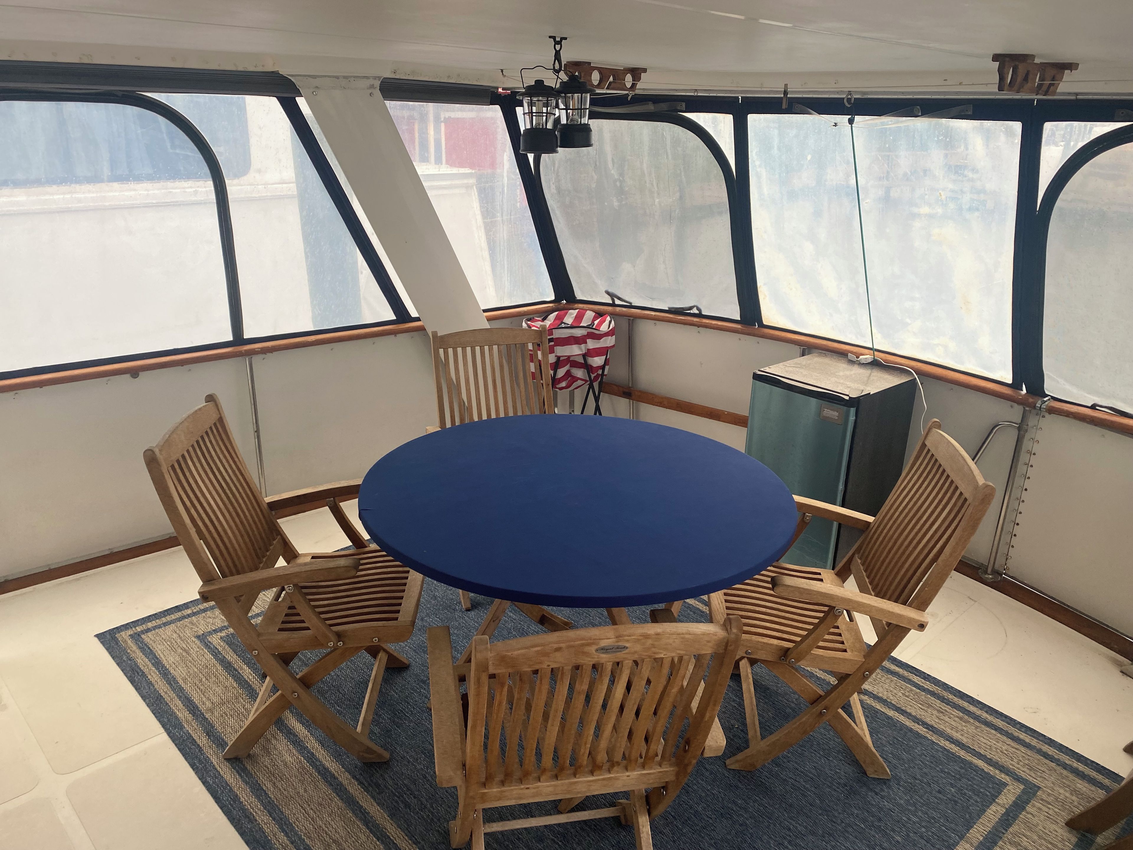Una mesa redonda con seis sillas de madera, un mantel azul y una alfombra estampada en una terraza con ventanas y un farol.