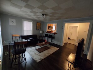 Una sala de estar con techo a cuadros, una mesa de comedor con sillas, un sofá y una zona de cocina con microondas.