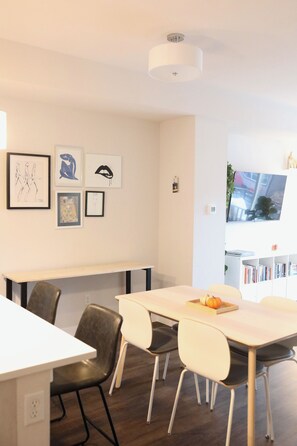 Un área de comedor moderna con una mesa blanca, sillas negras y una lámpara de techo blanca.
