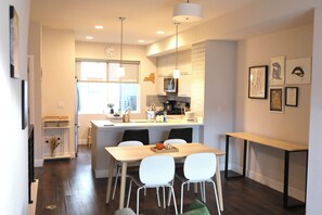 Una cocina moderna con una isla central, sillas blancas y una mesa de comedor.