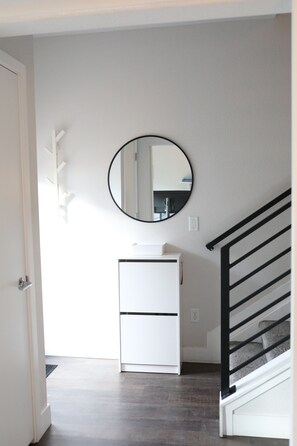 A hallway with a white refrigerator, a round mirror on the wall, and a staircase with black railings. - Modern 2BR/2.5BA Townhouse w/ dedicated Office, PET FRIENDLY near Sloans Lake (Lakewood)