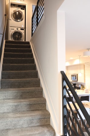 A staircase leading to a laundry area with a washing machine and dryer, a kitchen with modern appliances, and a dining area with chairs and a table. - Modern 2BR/2.5BA Townhouse w/ dedicated Office, PET FRIENDLY near Sloans Lake (Lakewood)