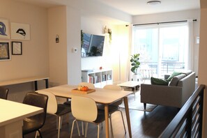 Una sala de estar moderna con comedor, un sofá, un televisor montado en la pared y una estantería.