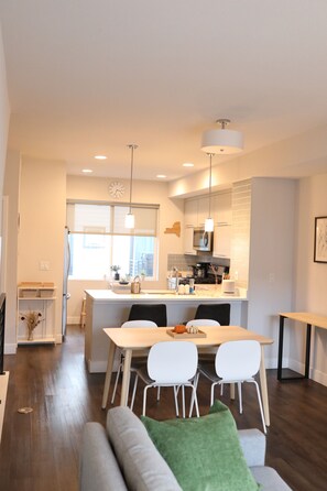 Une cuisine moderne avec un îlot central, un coin repas avec des chaises et un canapé agrémenté d’un coussin vert.