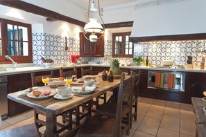 A kitchen with a wooden table set for breakfast, a coffee machine, and various breakfast items. - Masia Pairal - Luxury 11-Bedroom Villa near Sitges with Pool & Gardens (Can Macià)