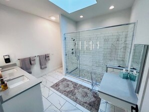 Une salle de bain moderne avec une douche à parois de verre, un grand miroir et une fenêtre de toit.