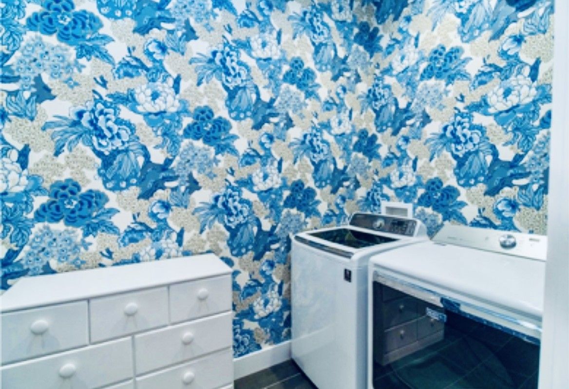 A laundry room with a white washing machine and dryer, a white cabinet with drawers, and a floral-patterned wall.
