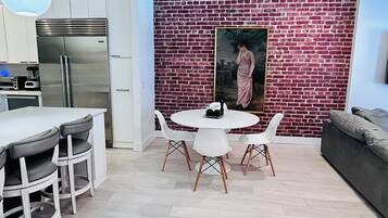 Una cocina moderna con refrigerador de acero inoxidable, armarios blancos y una pared de ladrillo con un cuadro enmarcado.