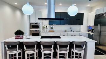 Una cocina moderna con una isla central, taburetes de bar, electrodomésticos de acero inoxidable e iluminación colgante.