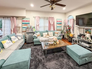 A living room with a sofa set, a coffee table, a television, and a ceiling fan.