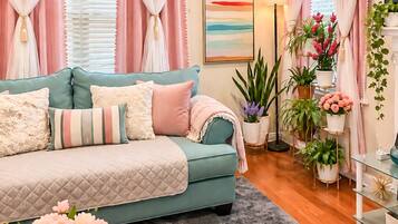 A living room with a teal sofa, pink curtains, and a painting on the wall.