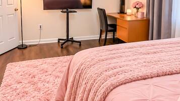 A bedroom with a large bed, a desk, a chair, a television, and a floor lamp.