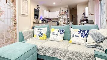 A living room with a teal sofa, a grey furry rug, and decorative pillows with text.