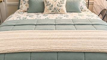 A bed with a floral patterned duvet and pillows, a knitted throw blanket, and a wall-mounted light fixture.