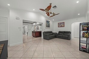 A spacious living room with a ceiling fan, two gray sofas, a wooden cabinet, and a bookshelf. - The Pool House | Spa, Game Room & Home Gym (Cape Coral)