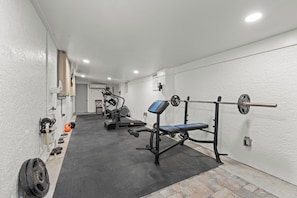 A gym with weightlifting equipment, treadmills, and a bench. - The Pool House | Spa, Game Room & Home Gym (Cape Coral)