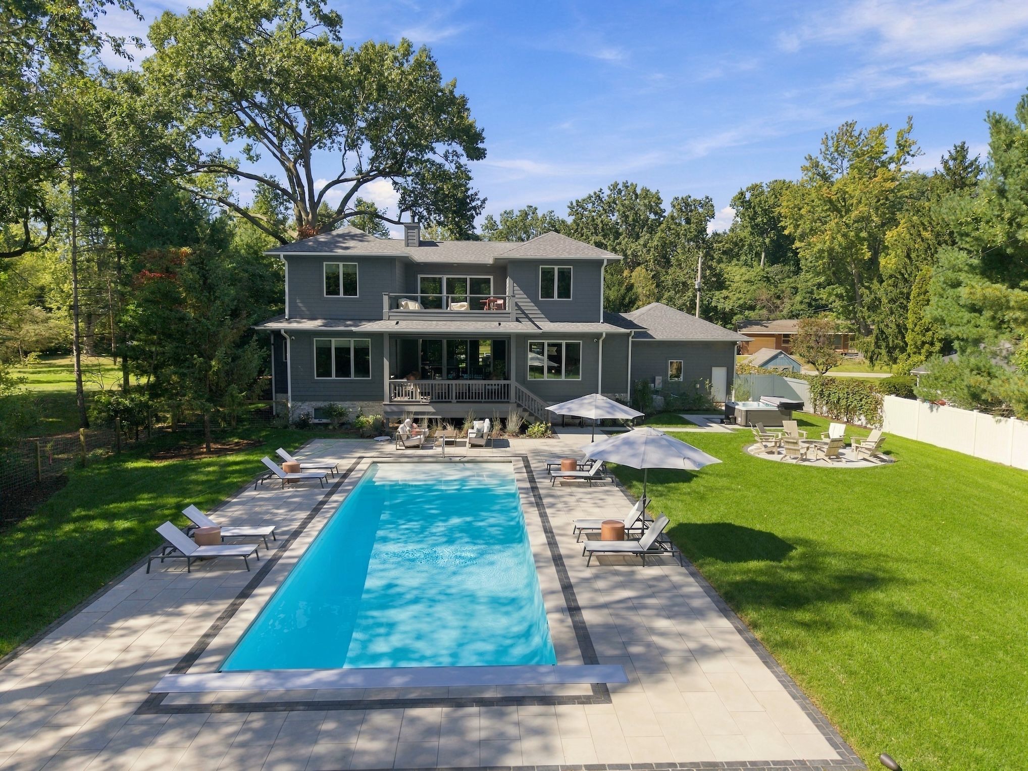 A two-story house with a swimming pool, outdoor seating, and a well-maintained lawn.