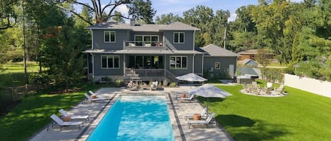 A two-story house with a swimming pool, outdoor seating, and a well-maintained lawn.