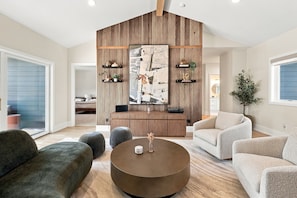 A modern living room with a round coffee table, grey sofas, and a wooden accent wall with shelves. - Luxury pool house with association beach access! (New Buffalo)
