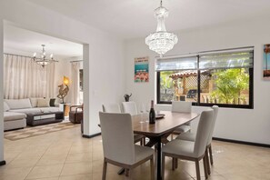 A dining area with a wooden table and chairs, a chandelier, and a view of the outdoors through a window. - The Golden Palm Villa (Noord)