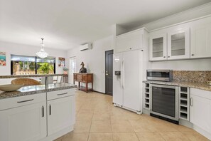A modern kitchen with white cabinetry, a granite countertop, a built-in microwave, and a refrigerator. - The Golden Palm Villa (Noord)
