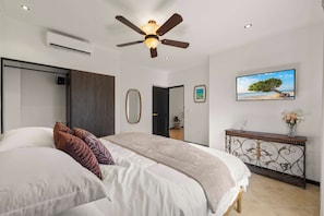 A bedroom with a bed, a ceiling fan, a TV, and a console table. - The Golden Palm Villa (Noord)