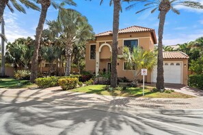 A residential building with a tiled roof, a garage, and a well-maintained garden with palm trees and shrubs. - The Golden Palm Villa (Noord)