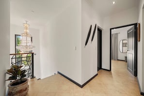 A hallway with a chandelier, a potted plant, and a door leading to another room. - The Golden Palm Villa (Noord)