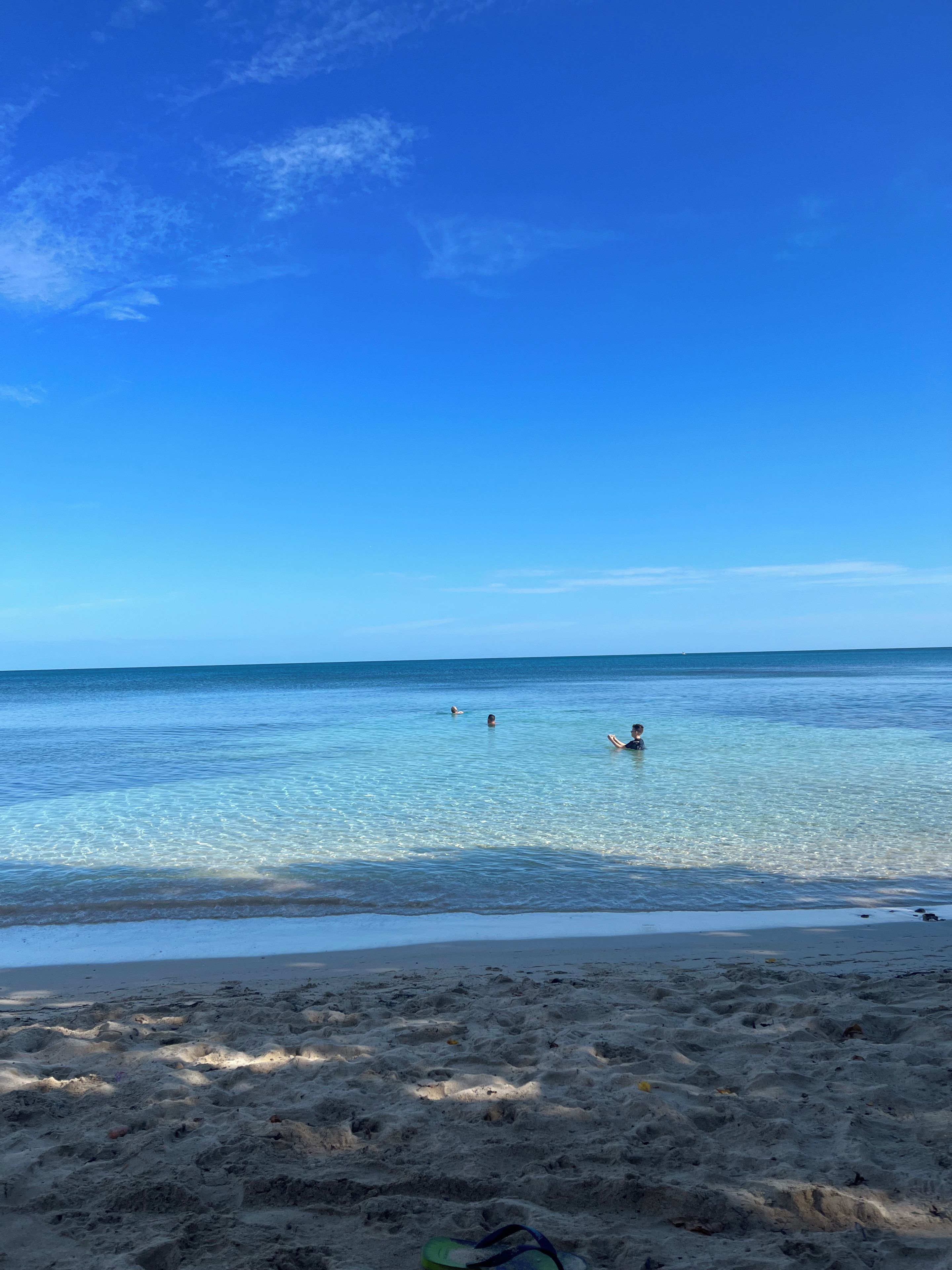 A beach with clear water, a sandy shore, and a few people swimming.