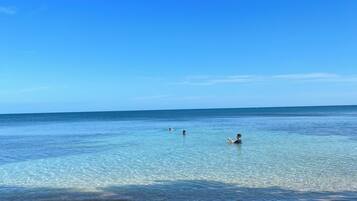 A beach with clear water, a sandy shore, and a few people swimming.
