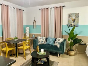 A living room with a sofa, a coffee table, a dining table with chairs, and a wall-mounted artwork. - Mountain Retreat with Boquerón Bay Views & Heated Saltwater Pool - 3B (Cabo Rojo)