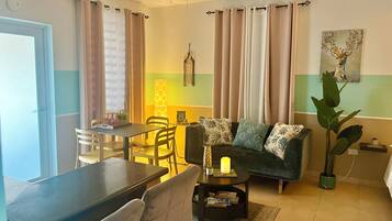 Una sala de estar con un sofá, una mesa de comedor con sillas, una lámpara y un cuadro en la pared.