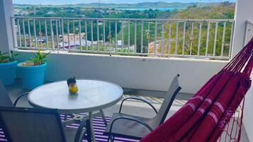 A balcony with a view of a cityscape, a round table with chairs, a hammock, and potted plants.