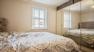A bedroom with a bed, two windows, a wardrobe, and a mirror.