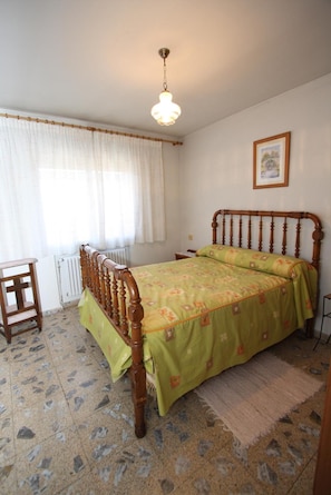 A bedroom with a wooden bed, a radiator, a window with curtains, and a picture on the wall. - Country House 'Casa Rural El Nido' (Solana de Ávila)