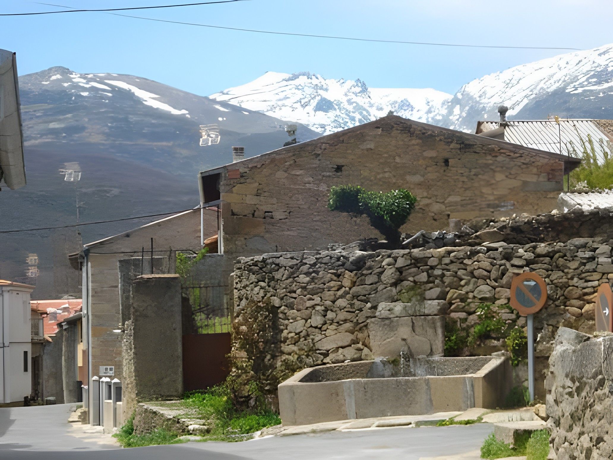 Un bâtiment en pierre avec un petit jardin, un portail en métal et une chaîne de montagnes en arrière-plan.