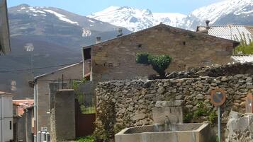Un bâtiment en pierre avec un petit jardin, un portail en métal et une chaîne de montagnes en arrière-plan.