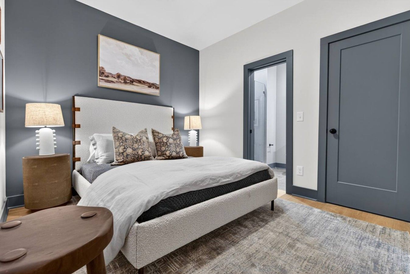 A bedroom with a bed, two bedside lamps, a nightstand, a rug, and a door.