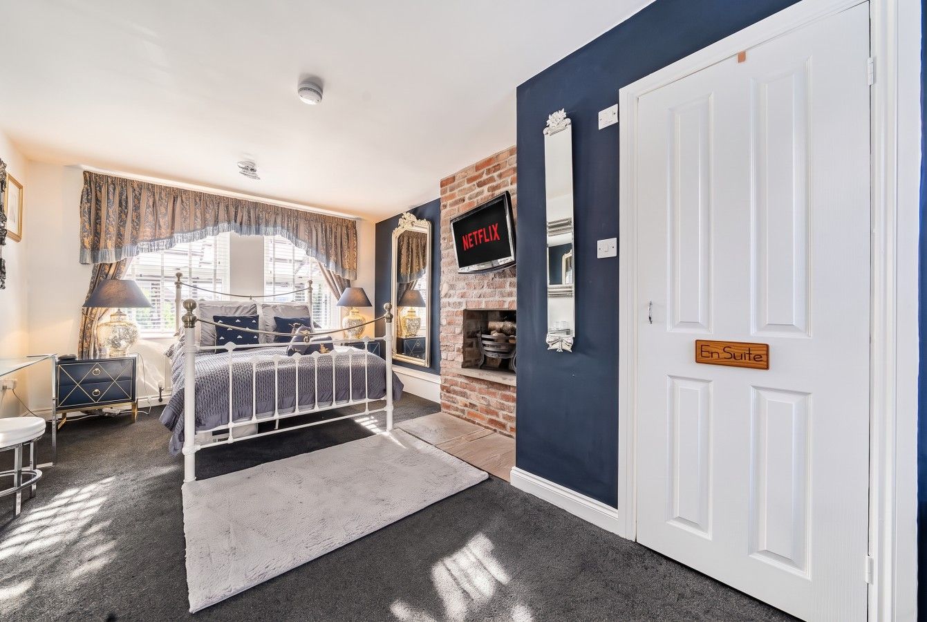 A bedroom with a bed, a television, a fireplace, and a door labeled 'En Suite.'